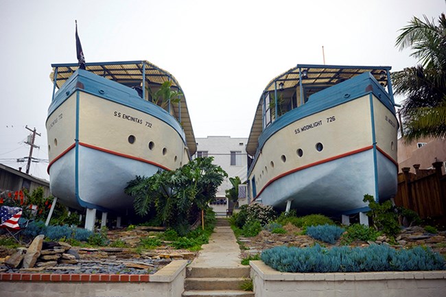 Image of two houses shaped like boats, with walkways, low walls, and plants.