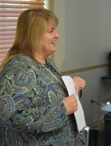 Profile view of white woman wearing a blue- green paisley shirt holding a piece of paper.