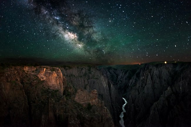 The Milky Way rises above sheer canyon cliffs at Black Canyon of the Gunnison National Park, Colorado