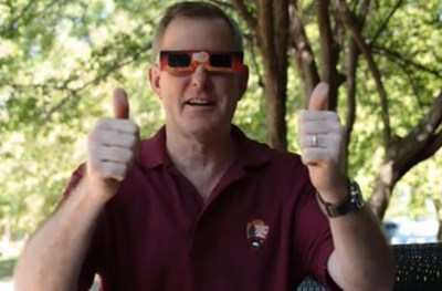 A man wears eclipse sunglasses and gives the thumbs up sign