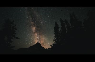 the milky way shines bright over a forested mountain
