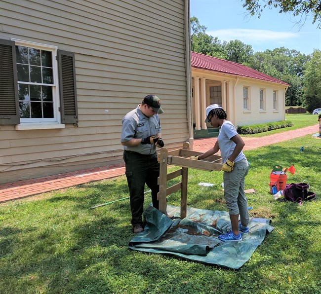 Two National Park Service staff using an archeology screen outside a historic building