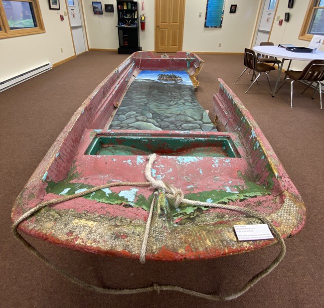 Boat debris painted with imagery of a lake and a forest.