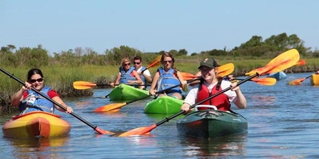 Ranger and visitors kayaking in marsh.