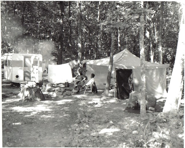 Two campers seated beside a tent and camper vehicle at Lewis Mountain Campground