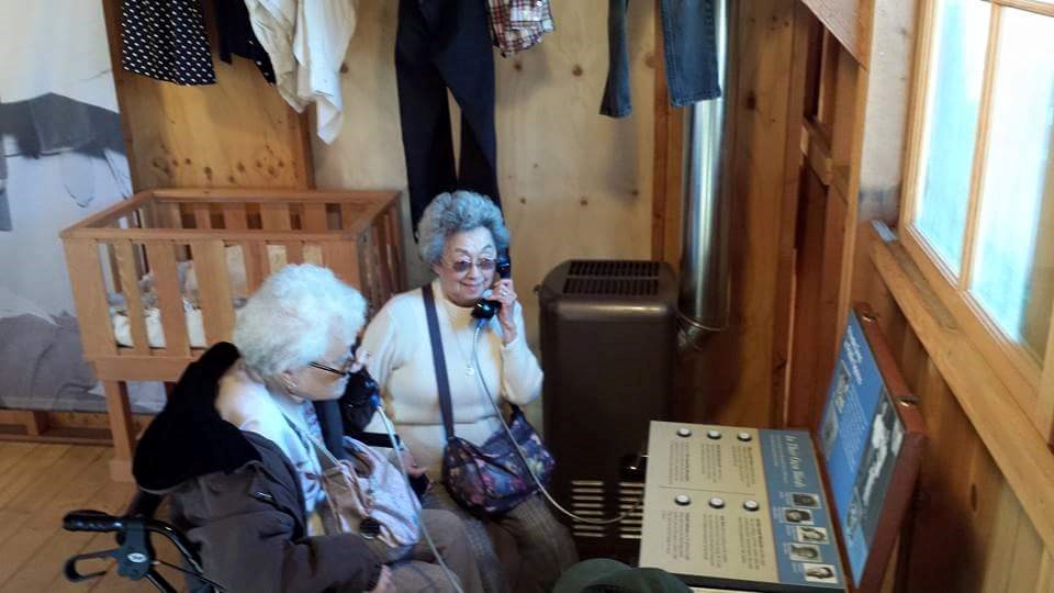 Two women hold phones to their ears in a museum exhibit inside a barracks