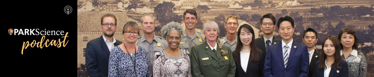 A group of people in NPS uniforms stand with others in front of a picture.