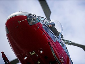 red helicopter hovers closely overhead with pilot staring out the window