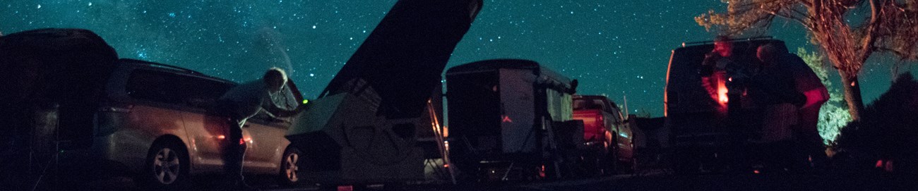 Visitors attending a star party in a national park, surrounded by vehicles and telescopes