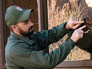 man in national park service uniform standing outside a building with two fingers touching a window