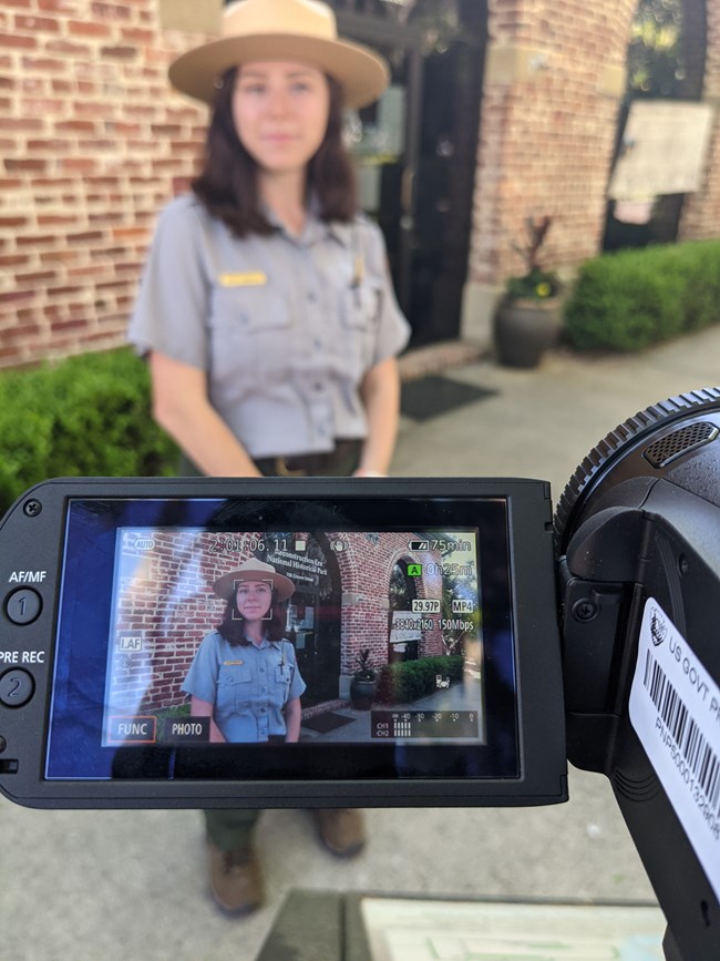 A ranger stands behind a video camera smiling.