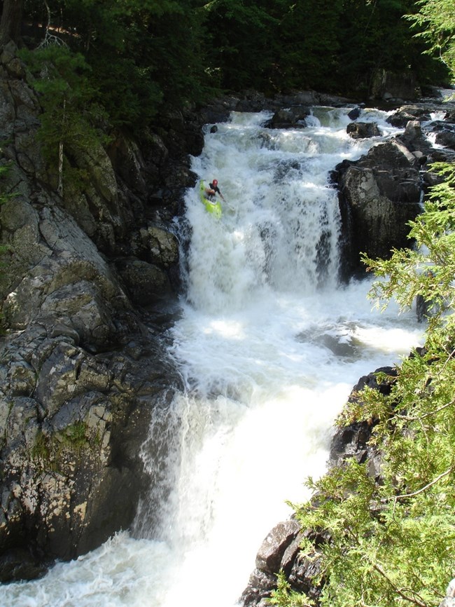 River flowing over tiered rock formation with paddler on yellow kayak goiung down the rocks