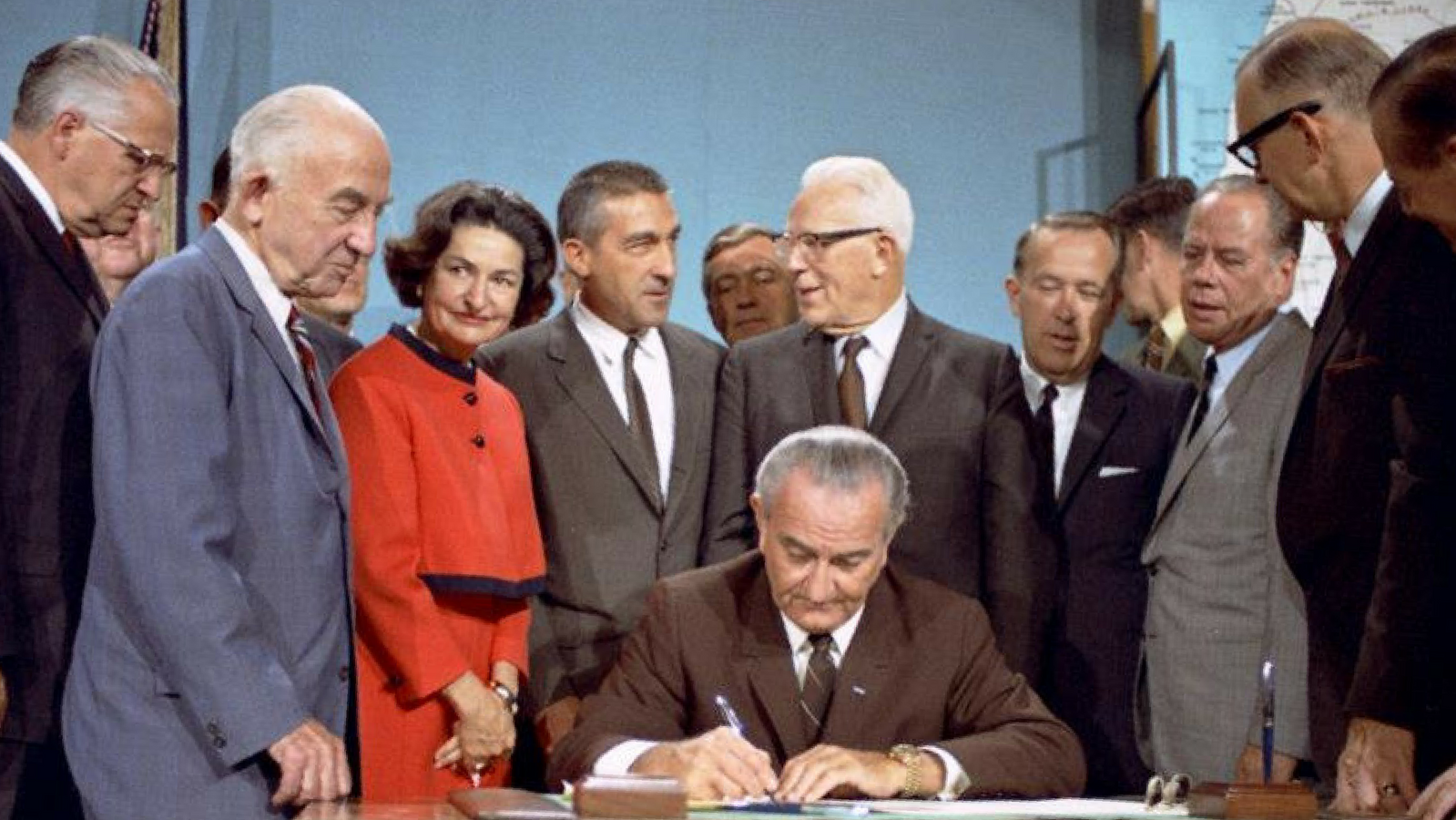 Lyndon B. Johnson sitting at a desk signing the Wild and Scenic Rivers Act surrounded by others standing around him