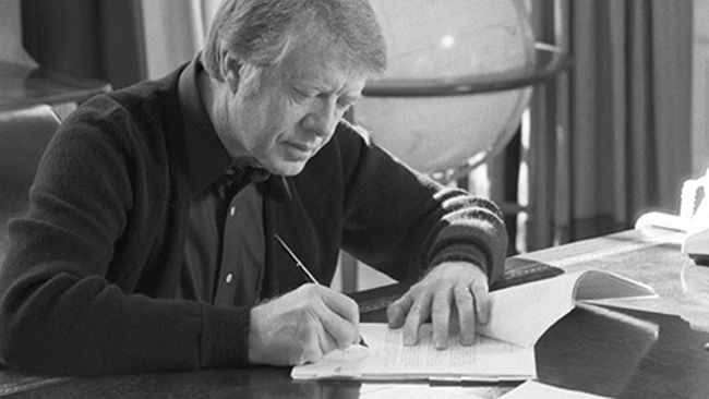 A black and white photo of Jimmy Carter signing the Presidential Memorandium.