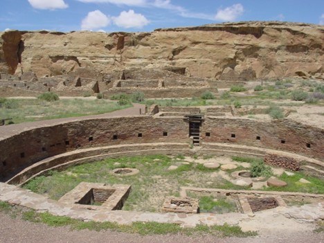 The great kiva in the plaza of Chetro Ketl. Tan sandstone ruins and cliffs.