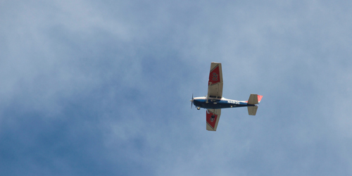 A red, white, and blue fixed-wing propeller plane flies in a blue sky