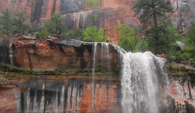 Frontal view of a waterfall over red rock framed by forest.