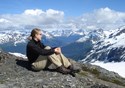 A female hiker sits atop a mountain and contemplates the quiet of her surroundings.