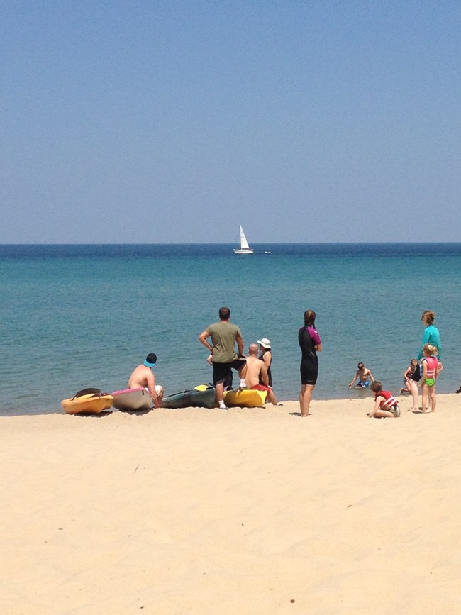 Kayakers and beach visitors watch a sailboat pass by offshore of Miners Beach.