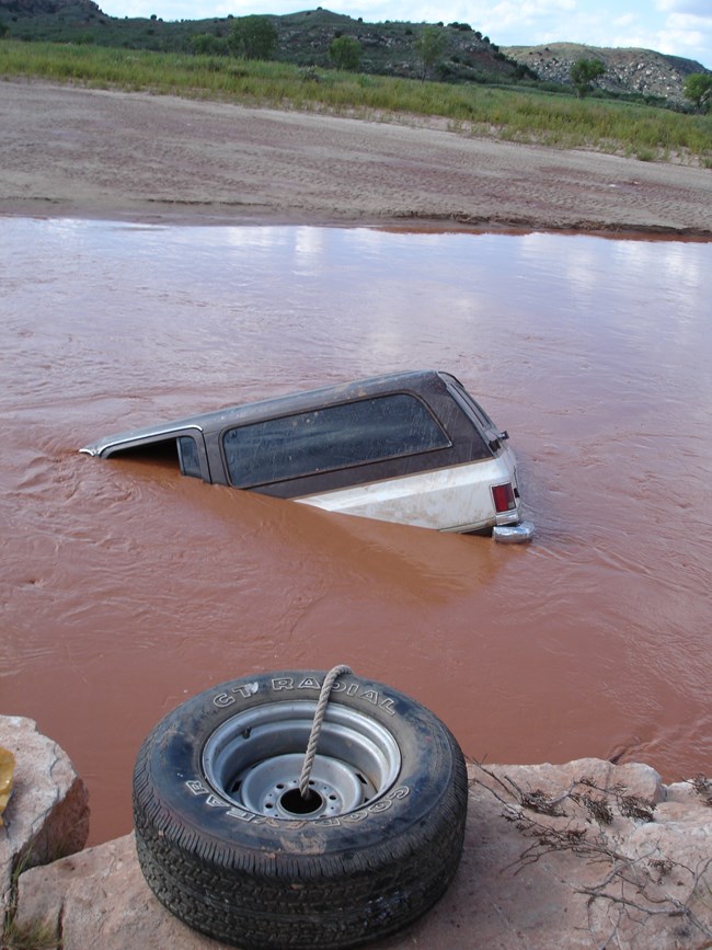 A vehicle is in a river and anchored with a tire.