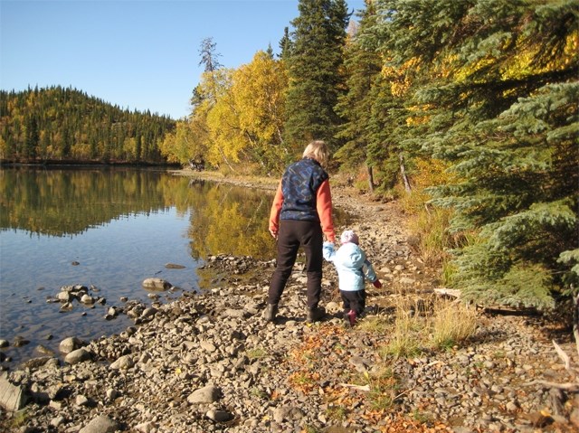 a woman holds a child's hand as they walk along a lakeshore in the fall