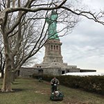 in front of statue of liberty and bare trees, man pushes soil aerator