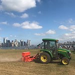 a green tractor drags a mower in front of city