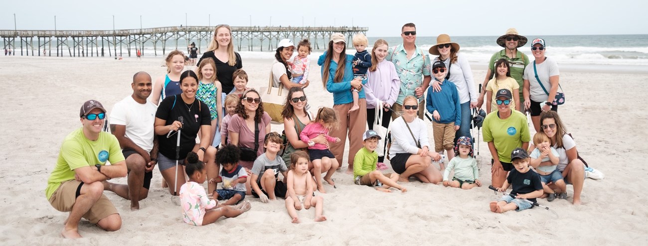 A couple dozen adults and children pose for a photo on an ocean beach.