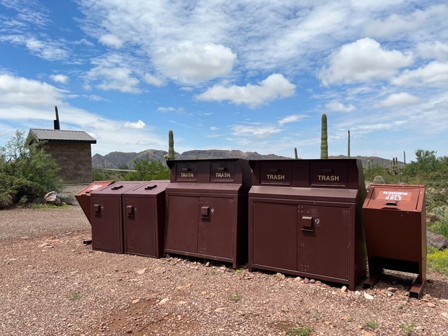 a row of animal resistant trash and recycling bins in a desert environment