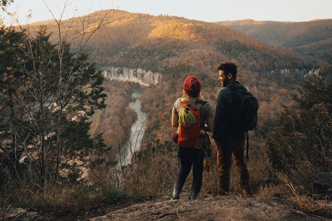 Two hikers view a river from a wide spot in the trail.