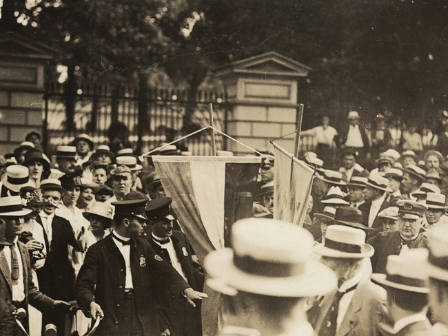 Police officers arrest an unseen person holding protest signs in a crowd of men