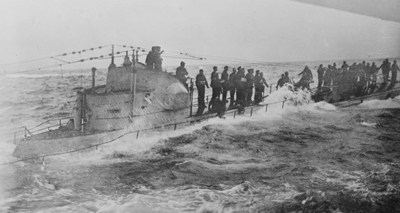 A German submarine crew stands on the deck as waves crash over the sides.