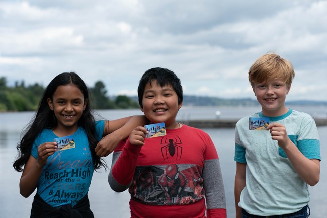 Three 4th grade students hold up Every Kid Outdoors passes