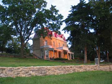 Image of the three story limestone mansion with the rays of sunrise hitting the front side