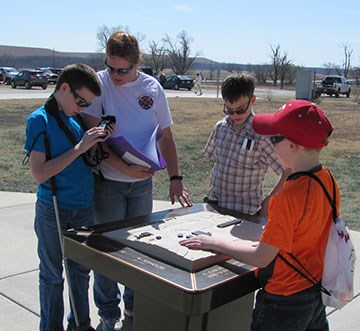 Four visitors using the Trekker Breeze unit while feeling the topographic tactile map of the ranch headquarters area. Map is located outside the visitor center.