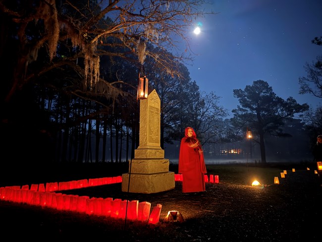 Woman standing by a monument surrounded by red luminaries.