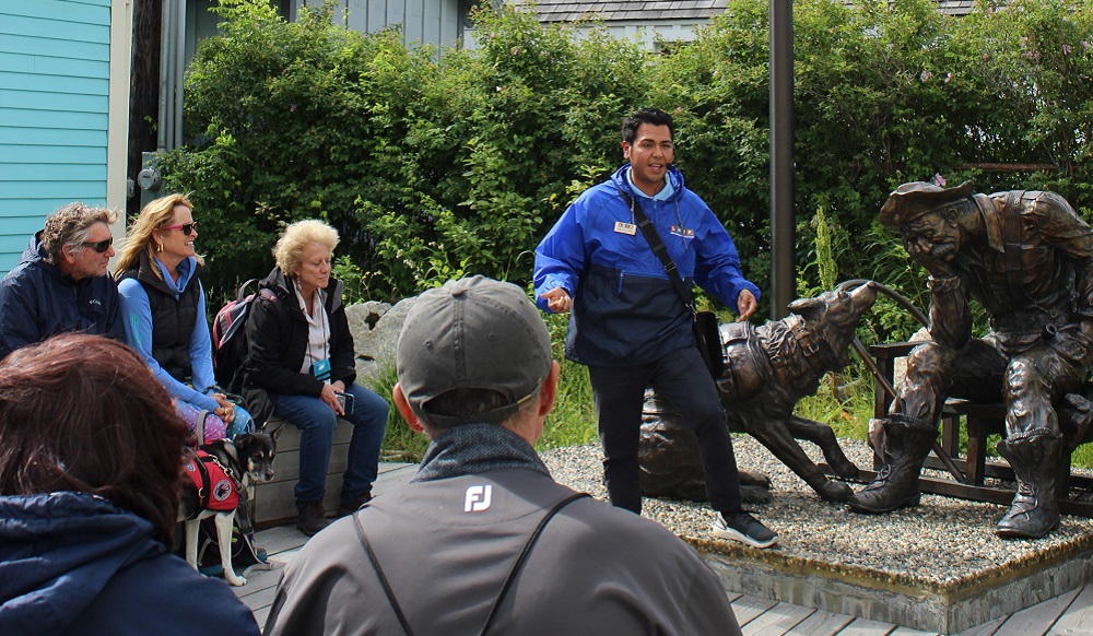 A group of people gather around the gold prospector statue during a historic walking tour