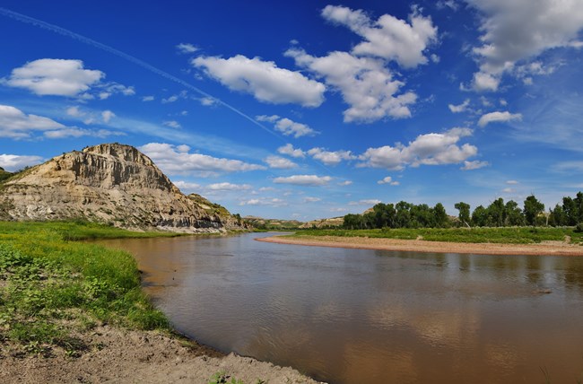 Blue sky with clouds and river winding through green grass.