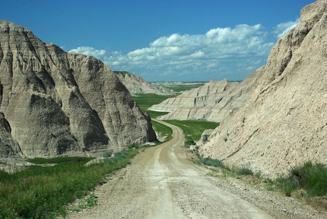 a dirt road leading down a hill weaves in and out of badlands formations