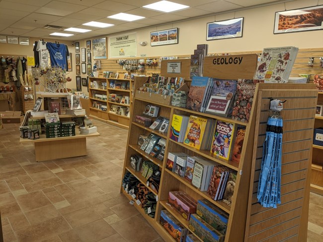 a bookstore selling books, bags, shirts, water bottles, and various souvenirs. A shelf in the foreground displays geology books and t-shirts hang in the background