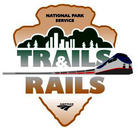 Trails & Rails logo with a National Park Service Arrowhead with an Amtrak train through the middle.