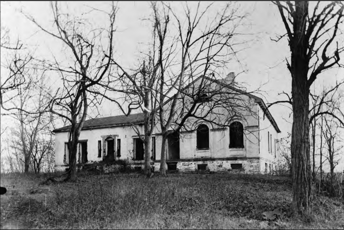 A black and white photograph of the ruins of the mason house surrounded trees with no leaves on them.