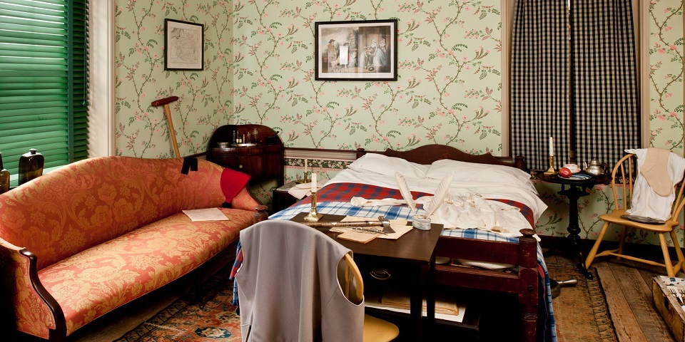 Color photo of a recreated 18th-century bedroom with green floral wallpaper and wooden furniture.
