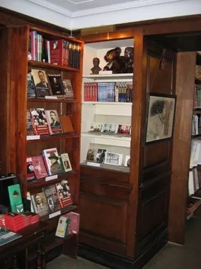 A picture of a wooden bookshelf built into the wall. Next to it is a table filled with books.