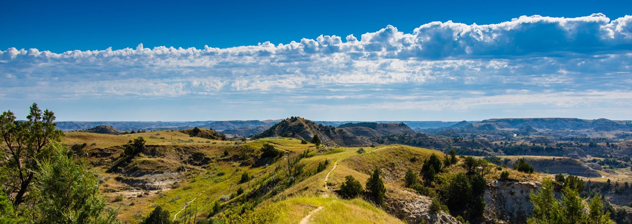 Trail through green prairie grasses following a ridge of a butte in badlands topography.