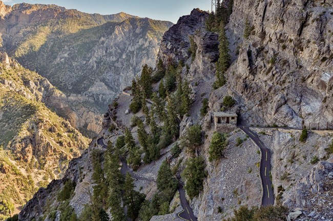 Steep paved switchbacks on a mountainside with an old rock buliding