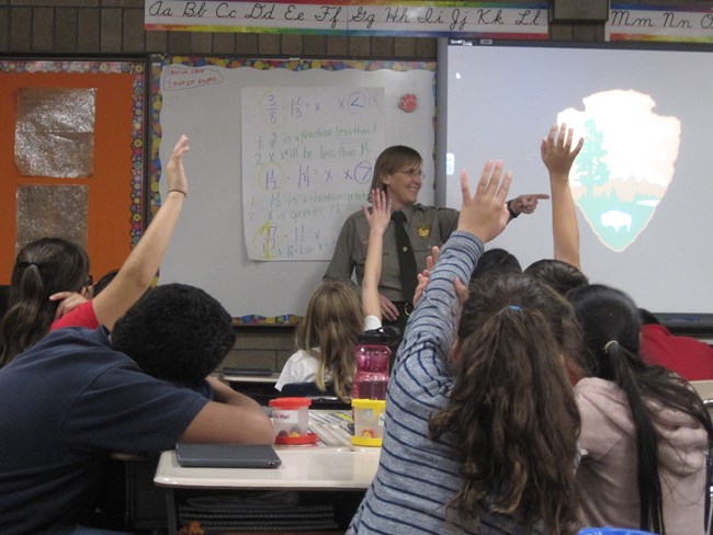Smiling ranger calls on child with raised hand in classroom setting