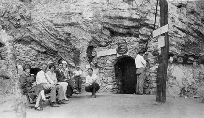 Multiple well dressed adults sit outside the cave entrance.