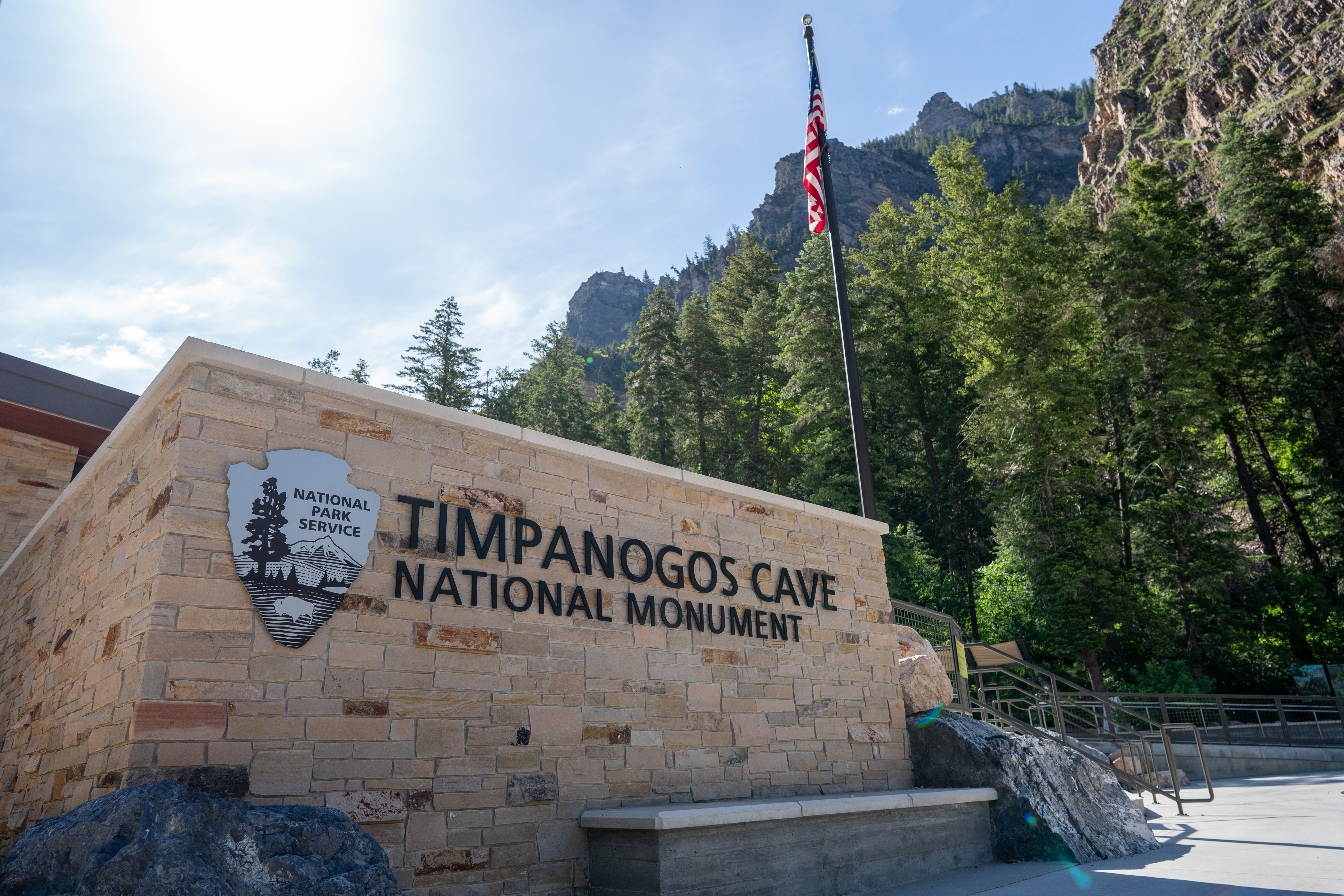 A silver National Park Service arrowhead by the sign reading "Timpanogos Cave National Monument"