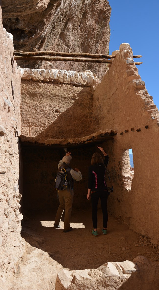 Two people in a cliff dwelling room looking at the roof structure